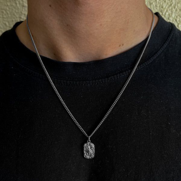 Person wearing a silver necklace with a pendant on a plain background